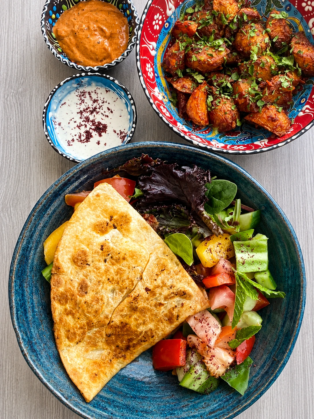 A Middle Eastern platter with filled flatbread, roasted potatoes, salad and sauces