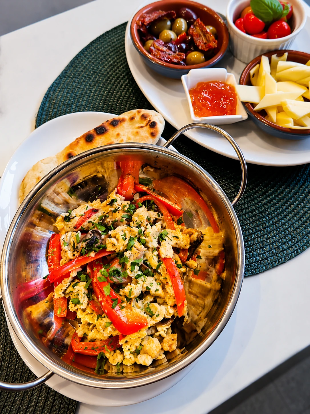 A breakfast pan with eggs, peppers and flatbread served with Middle Eastern sides